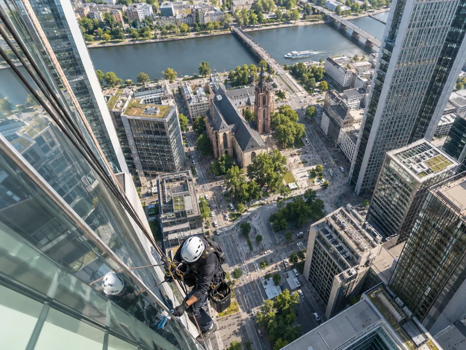 Blick von oben: Industriekletterer am Seil an einer Hochhaus-Glasfassade über der Frankfurter Innenstadt